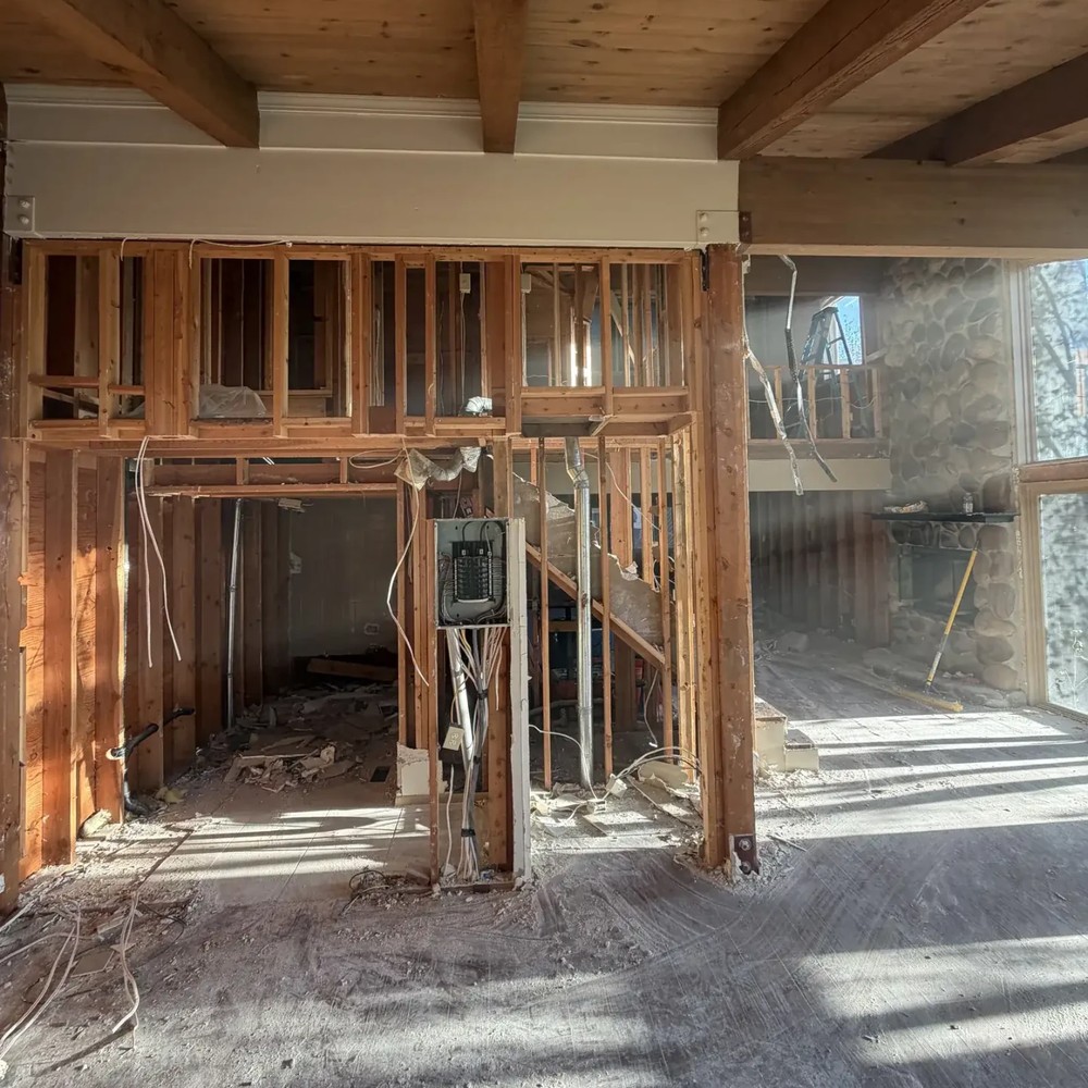 After: the same Park City space stripped to wall studs and ceiling decking, with the bathroom fixtures removed, debris on the subfloor and an open electrical panel